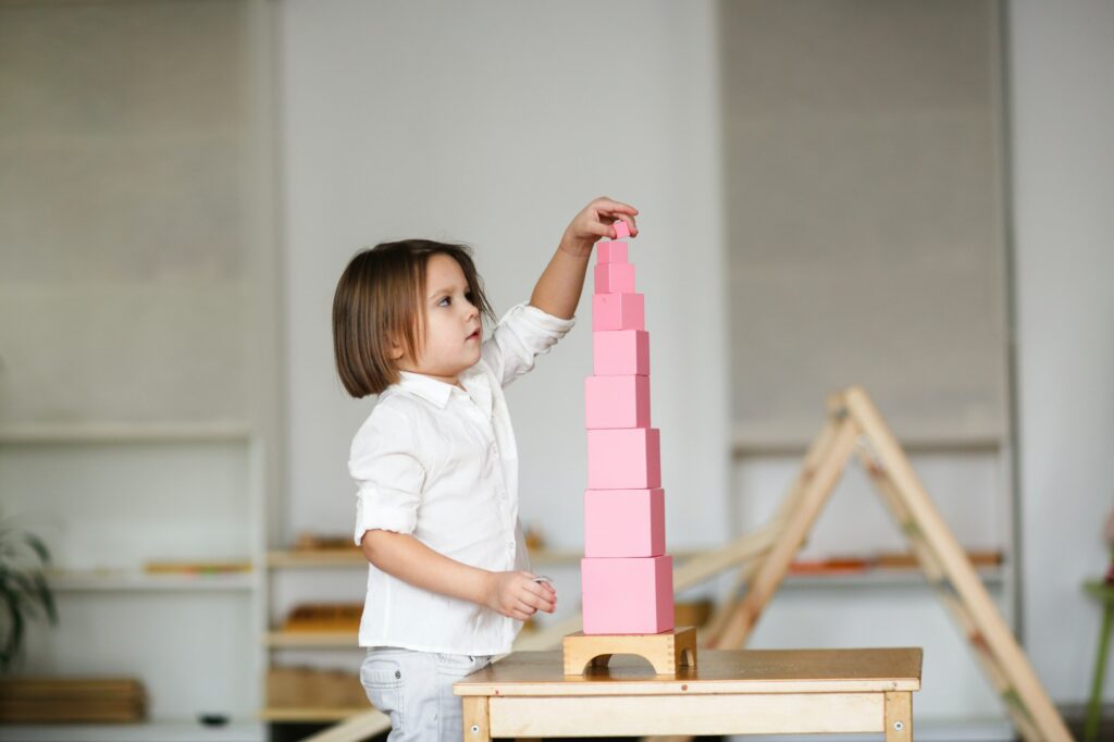 child girl playing with pink tower, developing sensory activities