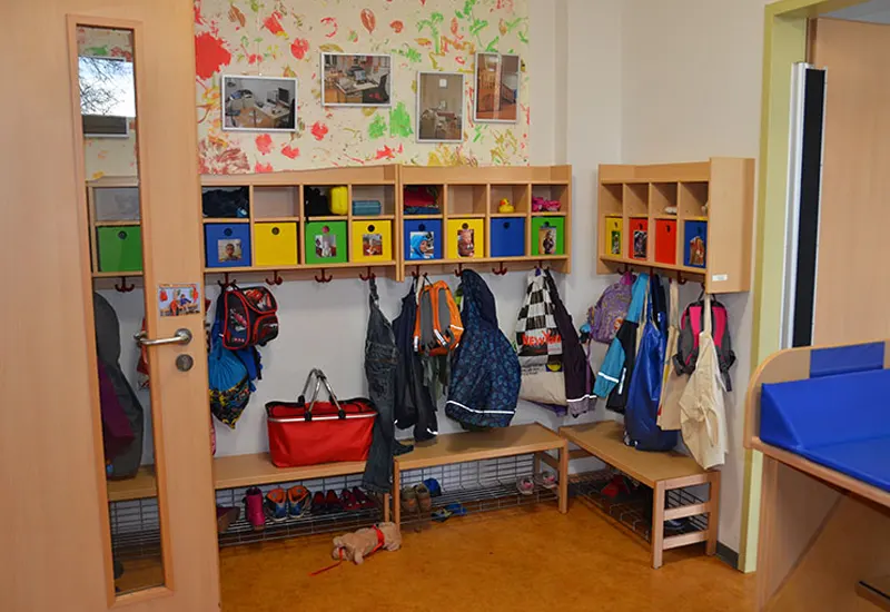 A colorful children's cloakroom with cubbies and hooks for bags and coats, benches for sitting, and various items stored neatly, in a well-organized classroom.
