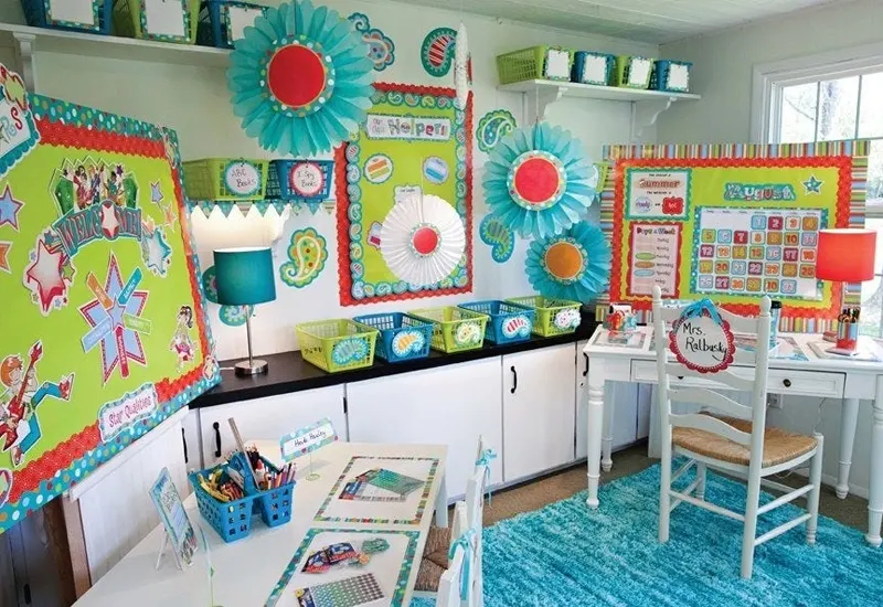The image shows a brightly decorated classroom display area. Colorful bulletin boards are filled with educational materials and decorations, including student work, learning activities, and motivational posters. Shelves and bins are neatly organized, holding various classroom supplies.